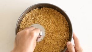 A Hand Pressing a Buttery Biscuit Crumb Mixture Evenly Into the Base of A Springform Pan