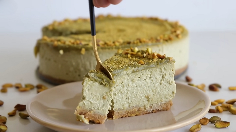 A Slice of Creamy Pistachio Cheesecake on A Plate, with A Fork Cutting Through It