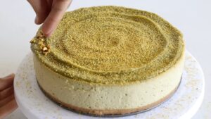 A Finished Pistachio Cheesecake Being Garnished with Chopped Pistachios on Top for An Elegant Presentation