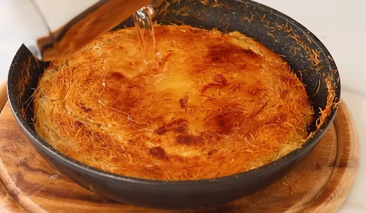 Golden baked kanafa in a pan with syrup being poured over the top