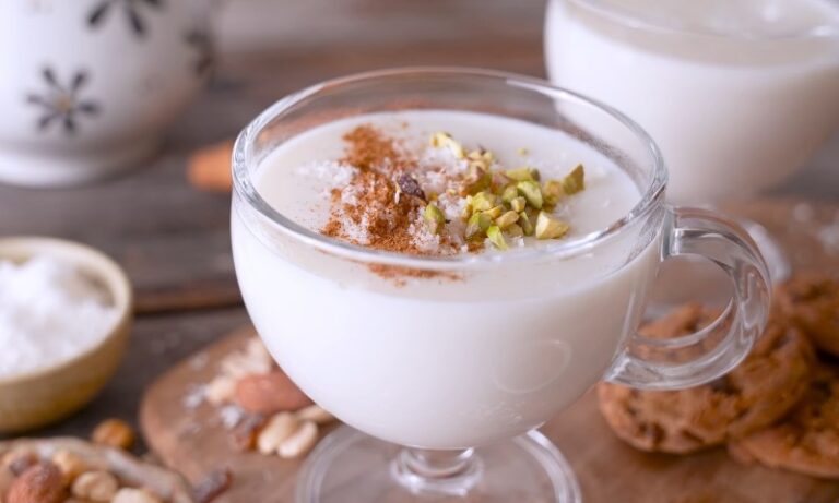 A glass cup filled with creamy beverage, topped with cinnamon and chopped pistachios