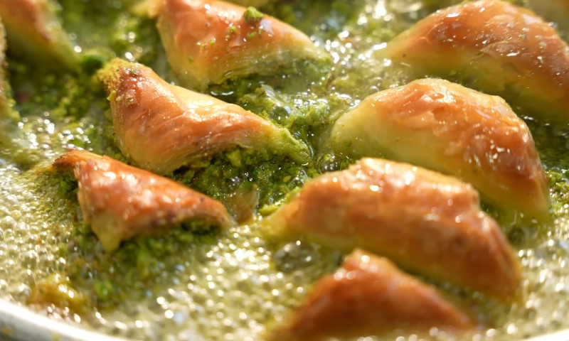 Golden-brown baklava pieces sizzling in hot oil, with vibrant green pistachio filling
