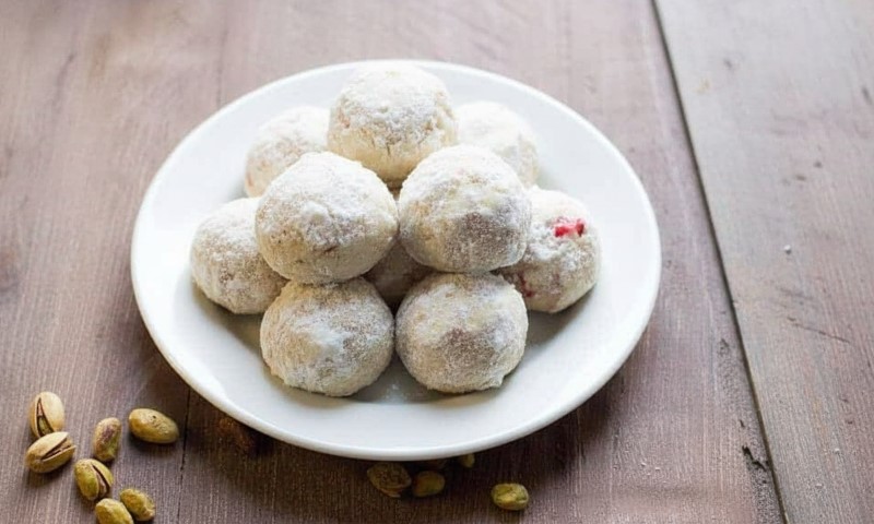 A white plate holds several round, snowball-like cookies dusted with powdered sugar, arranged on a wooden table