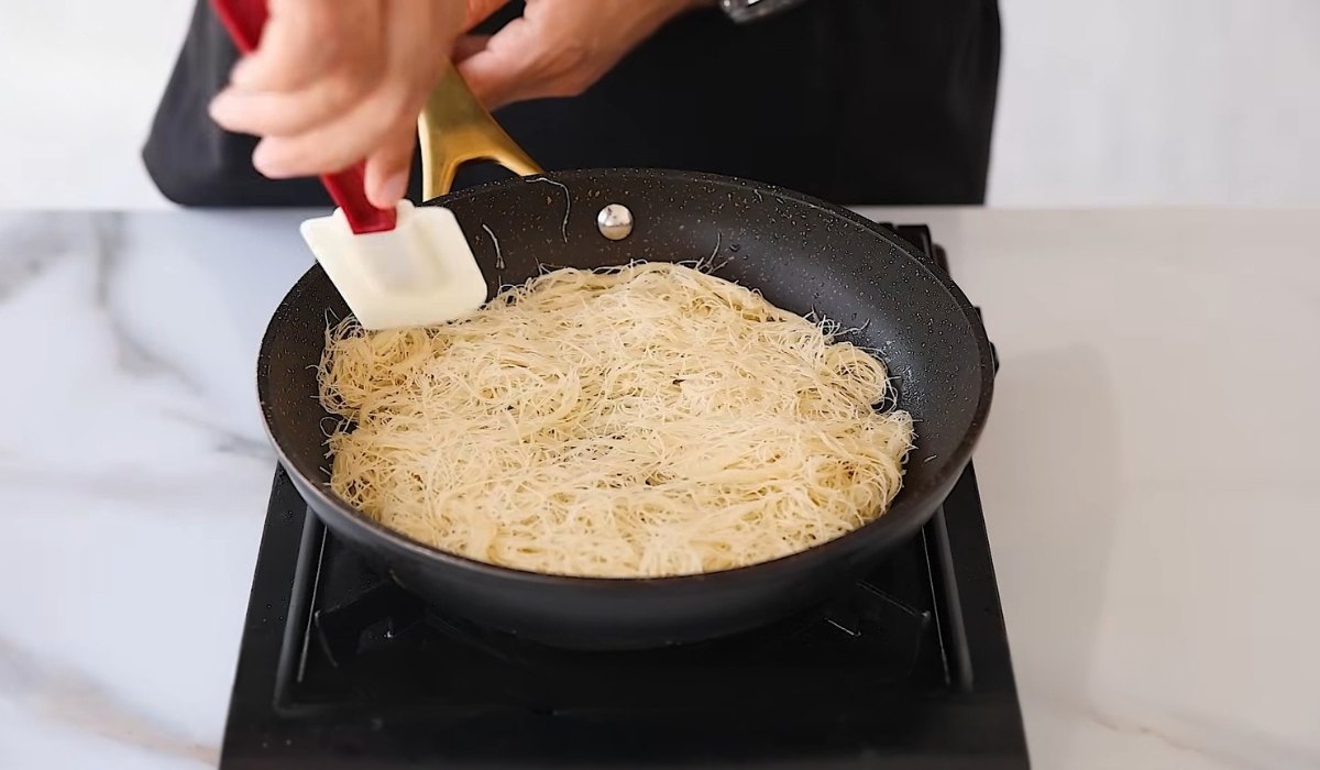 Shredded pastry being spread evenly in a pan for making kanafa