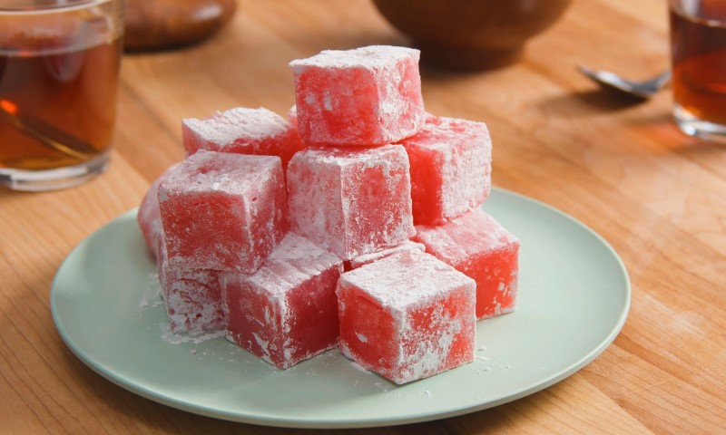 A stack of pink Turkish delight cubes dusted with powdered sugar sits on a light blue plate on a wooden table